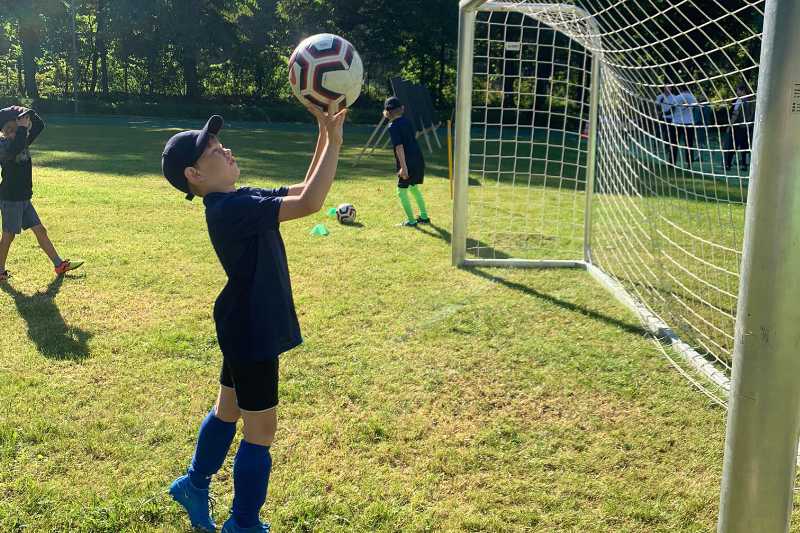 Junge mit Fußball in der Hand vor einem Tor auf dem Bolzplatz