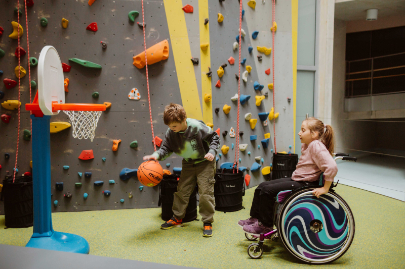 Zwei Kinder spielen Basketball vor einer Kletterwand