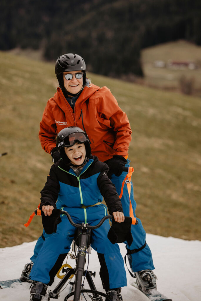 Zwei Personen mit Winterklamotten beim Skibob fahren