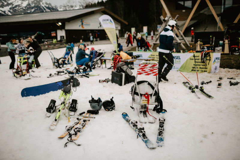 Vor Hütte liegen mehrere Skiausrüstungen an denen Personen stehen