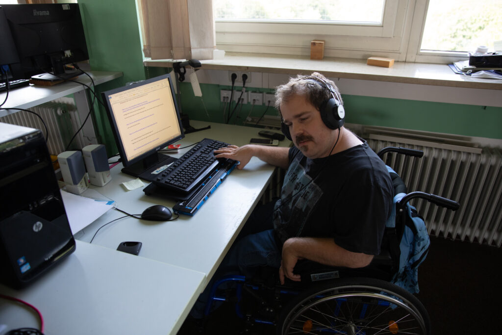 Mann im Rollstuhl arbeitet am Computer mit Brailezeile