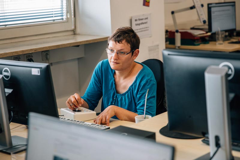 Frau arbeitet am Computer mit Spezialtastatur und Joystick-Mouse