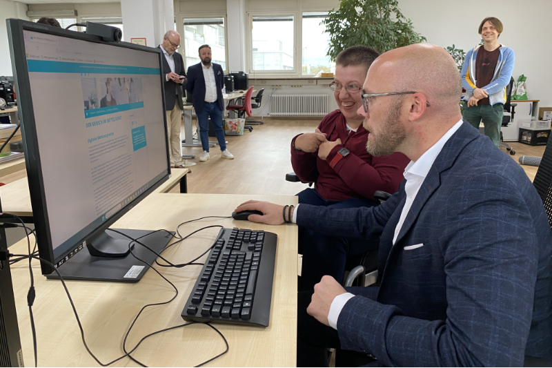 Werkstattbeschäftigte und Staatsminister für Digitales schauen sich eine Webseite an