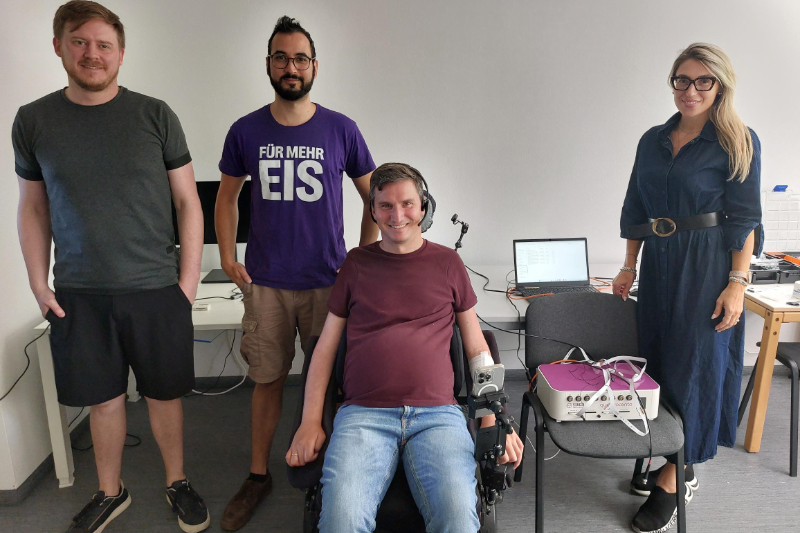 Eine Wissenschaftlerin, ein Rollstuhlfahrer und zwei Wissenschaftler lächeln in die Kamera
