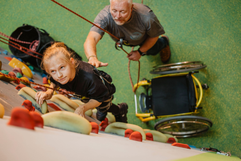 Mädchen klettert an Seil gesichert mit Helfer an Kletterwand