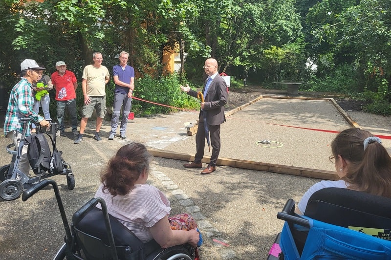 Personen beobachten die Eröffnung der neuen inklusiven Boule-Bahn durch Vorstand Ernst-August von Moreau.
