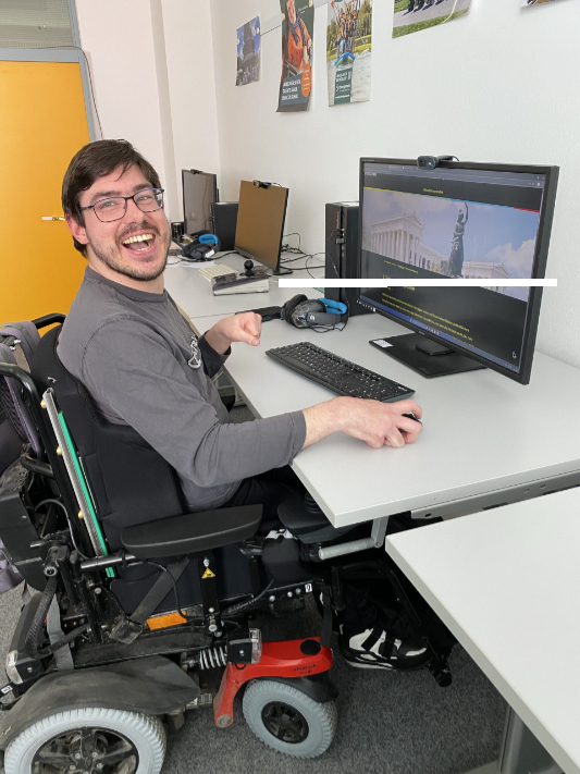 Mann im Rollstuhl am Computerarbeitsplatz. Auf dem Monitor Seite Sehenswürdigkeiten