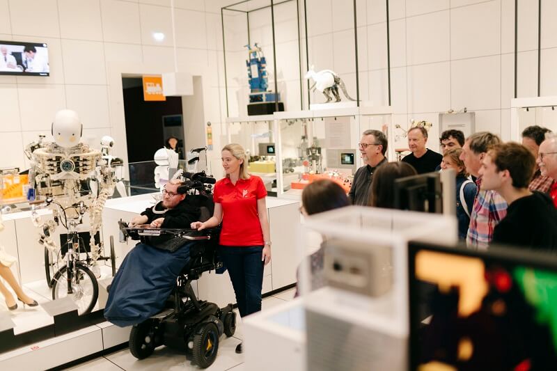 Rundgang von Museumsführern mit und ohne Behinderung im Hintergrund Zuhörer*innen.