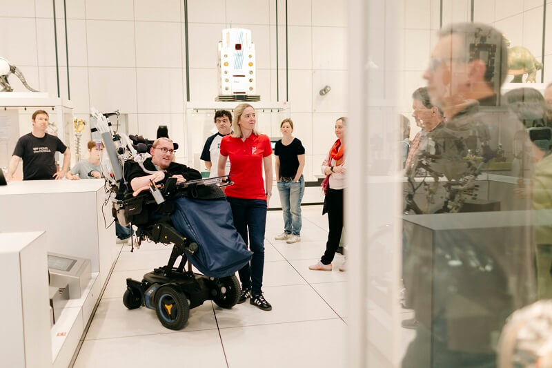 Rundgang von Museumsführern mit und ohne Behinderung, im Hintergrund Zuhörer*innen