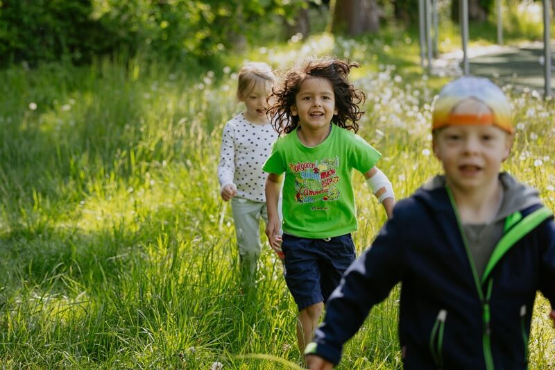 Kinder hintereinander auf einer Wiese laufend