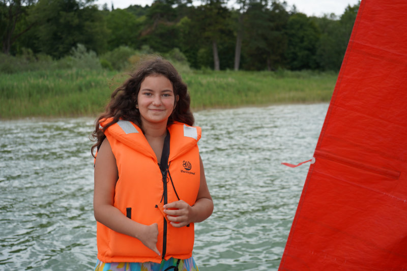 Frau mit Rettungsweste und Segelboot auf dem See