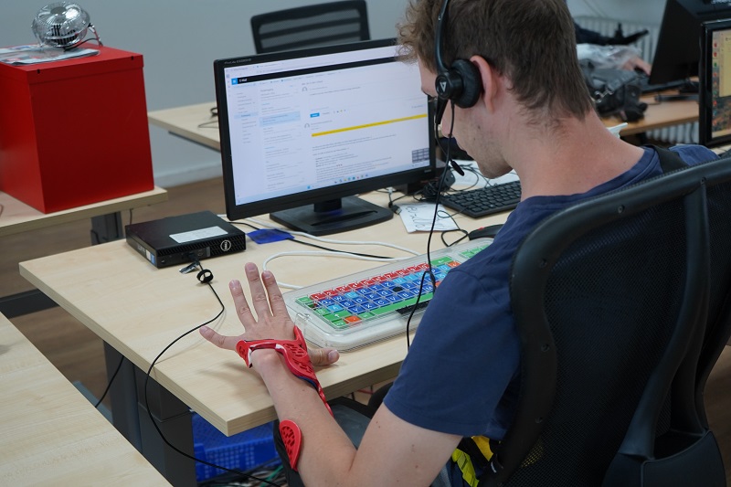 Mann sitzt an Computerarbeitsplatz mit Kleinfeldtastatur und Kopfhörer