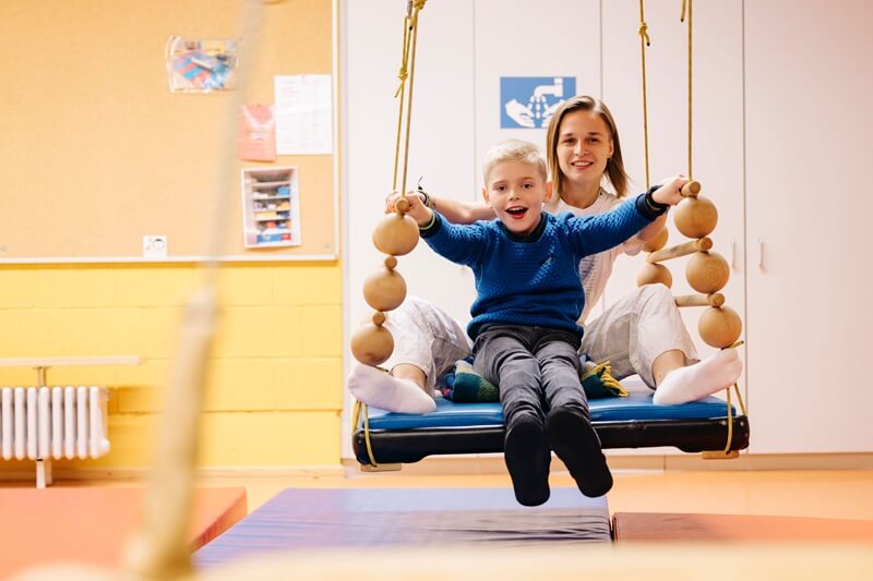 Tommy mit seiner Therapeutin in einer Therapieschaukel: damit es weitergeht!