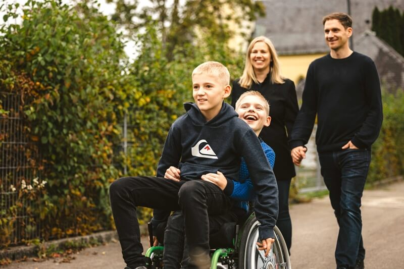Tommy und sein Bruder im Rollstuhl sitzend, dahinter die Eltern: damit es weitergeht!
