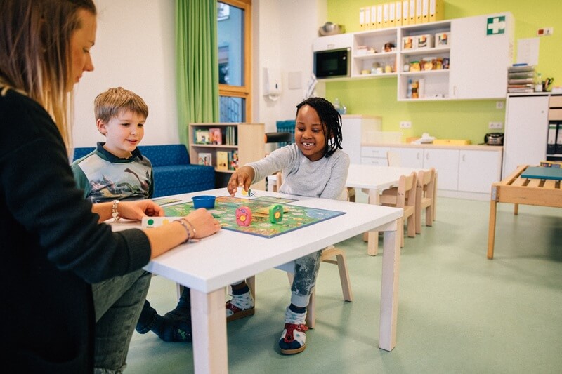 Erzieherin spielt mit zwei Kindern ein Brettspiel.