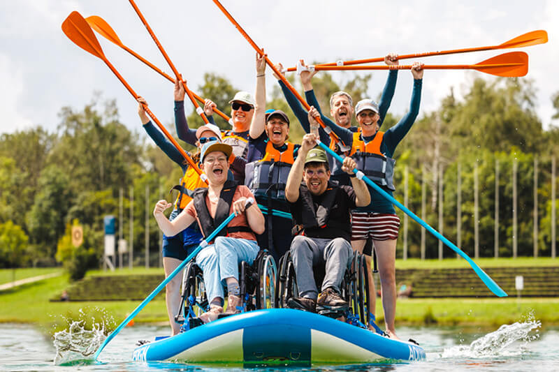 Mehrere Personen mit und ohne Behinderung auf einem SUP