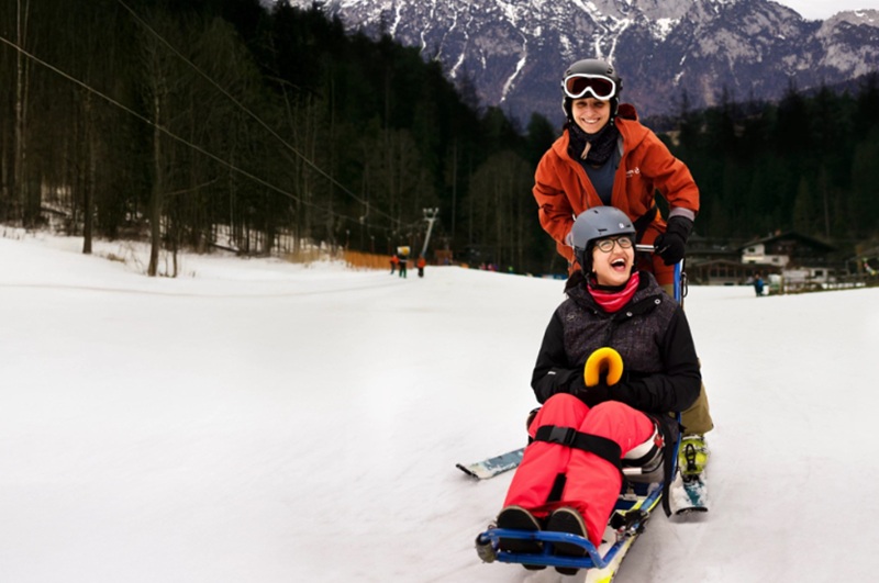 Skifahrerinnen mit Dualski-Bob in Winterlandschaft.