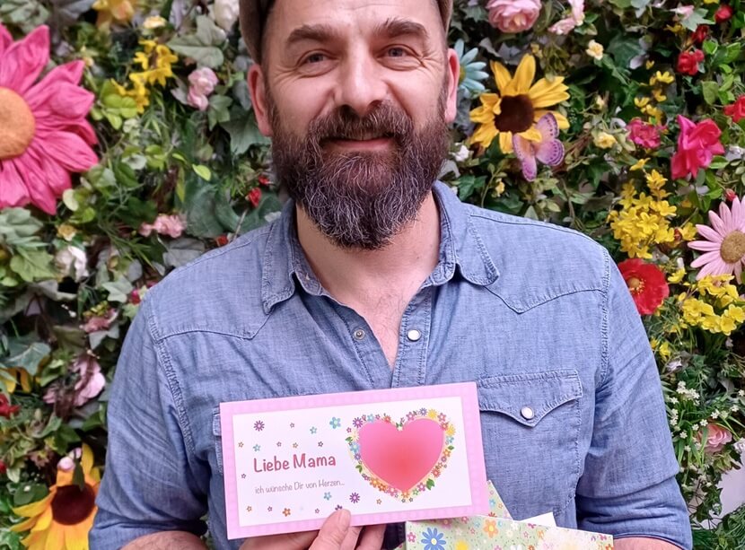 Mann hält Karte in der Hand Text: Liebe Mama ich wünsche Dir von Herzen