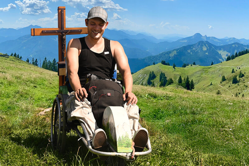 Person im Rollstuhl neben Gipfelkreuz