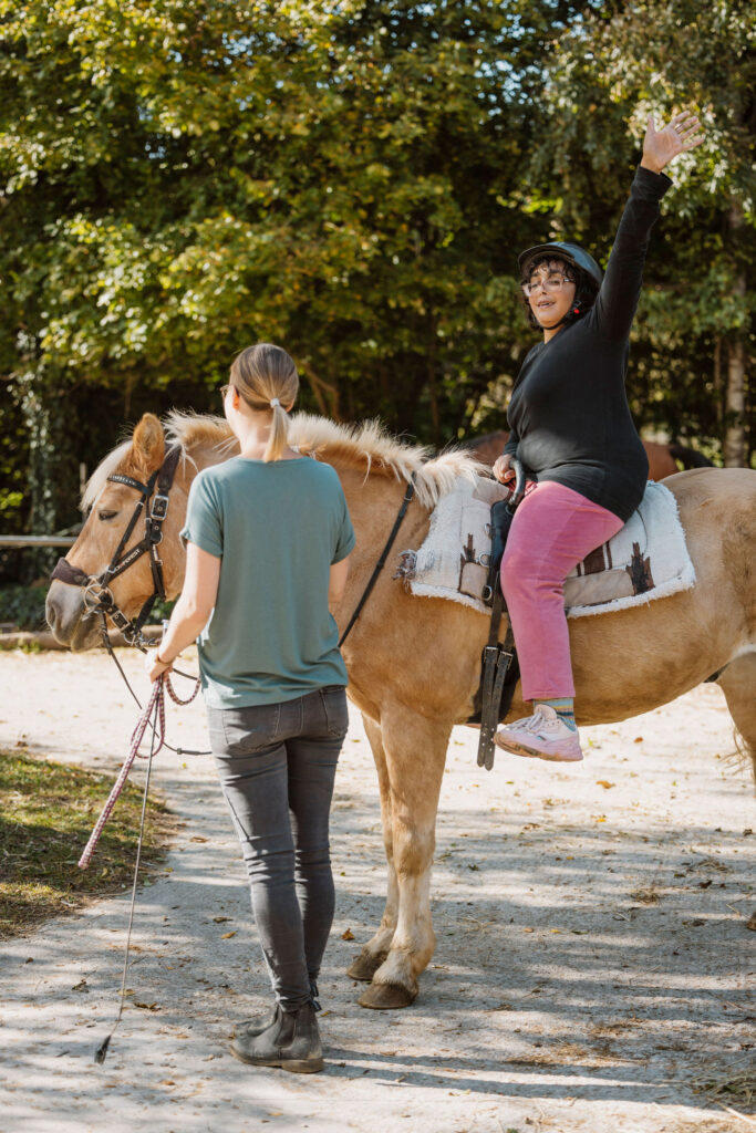 Frau sitzt in Siegerpose auf einem Pferd, Assistentin hält Zügel in der Hand