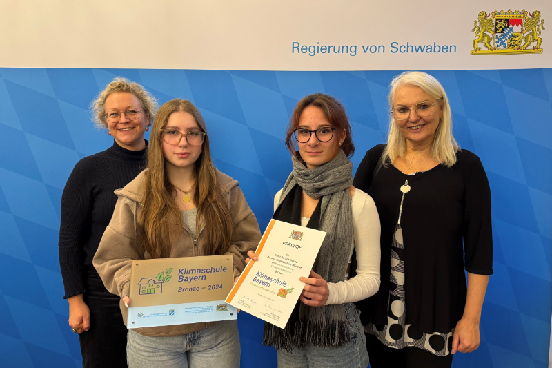Text: Regierung von Schwaben Mehrere Personen stehen nebeneinander und haben Bronzene Plakette und Urkunde in der Hand