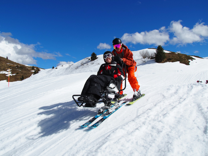 Zwei Personen in Skiausrüstung fahren Piste hinab